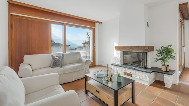 Una sala de estar con sofá, mesa de centro, chimenea y ventanas amplias.