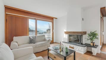 Ein Wohnzimmer mit einer Couch, einem Couchtisch, einem Kamin und großen Fenstern.