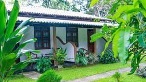Une maison traditionnelle avec un toit en tuiles, entourée d’une végétation luxuriante et d’une pelouse bien entretenue.