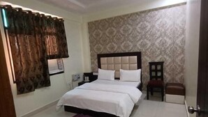 A bedroom with a bed, a ceiling fan, a nightstand, a chair, and a small table. - Hotel Heritage Villa By MNG Rooms (Kanpur)