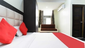 A hotel room with a bed, red pillows, a red carpet, a sofa, and a door. - Hotel Heritage Villa By MNG Rooms (Kanpur)