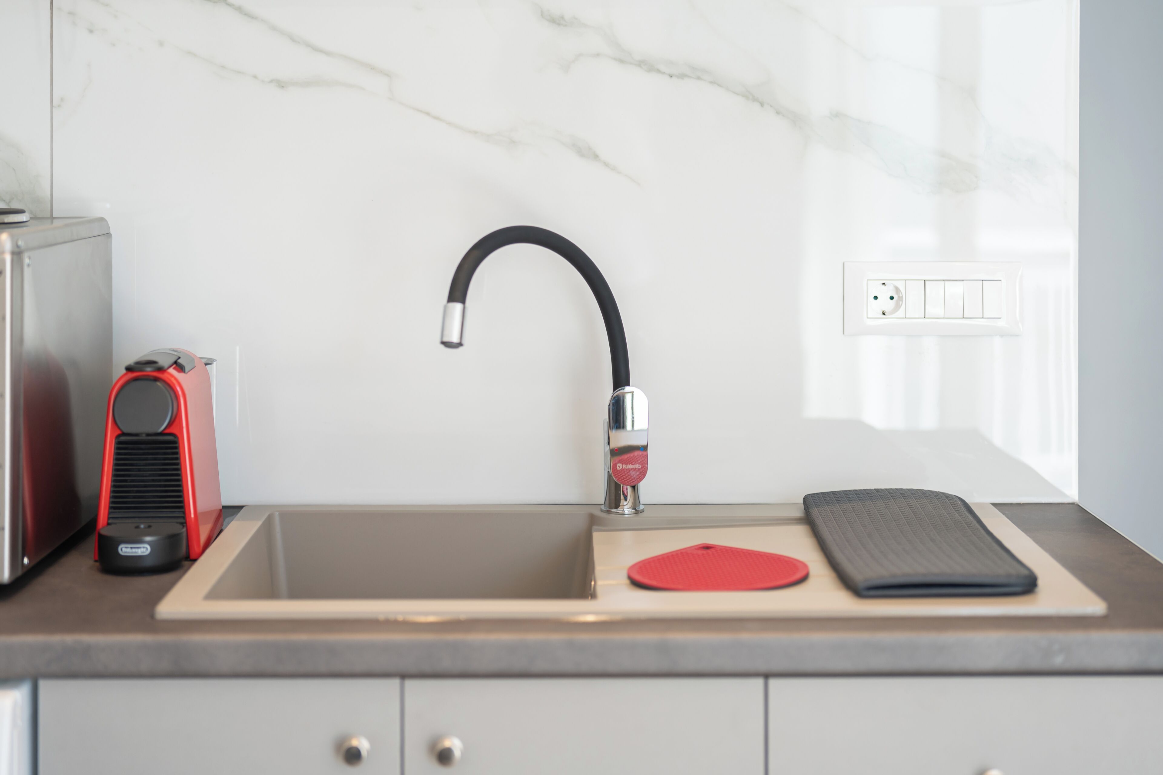 Una cocina con un grifo moderno, una tetera y un felpudo en la encimera.