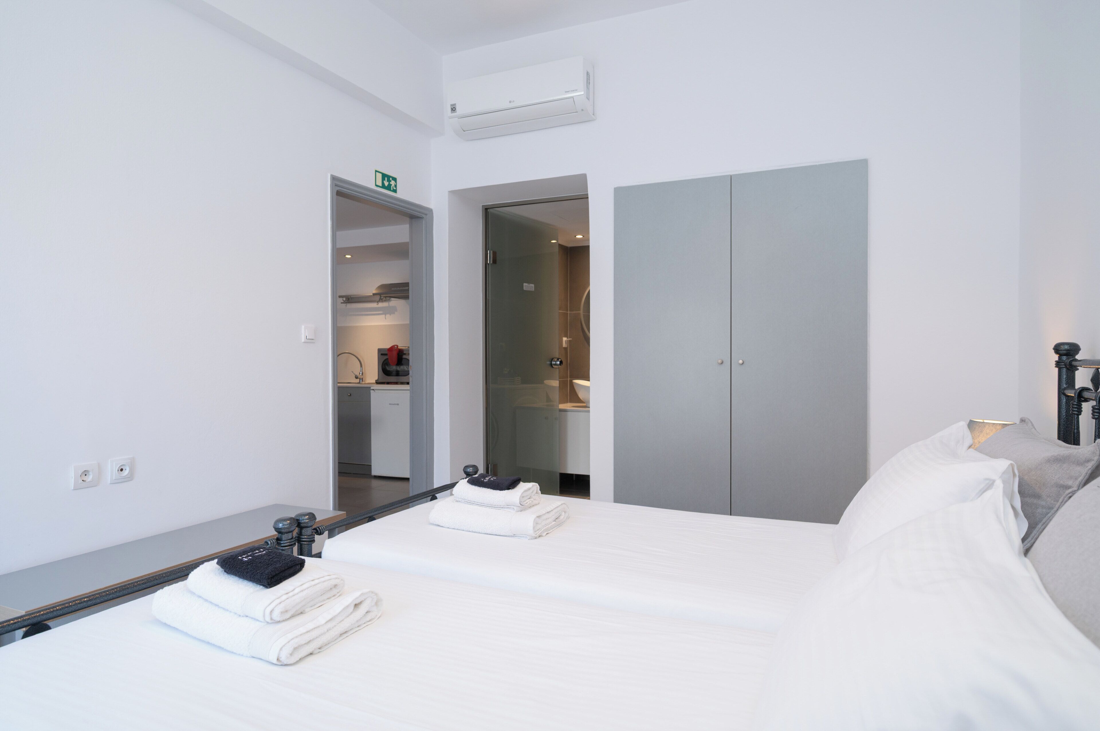Quarto de hotel com cama, armário, banheiro e cozinha compacta.