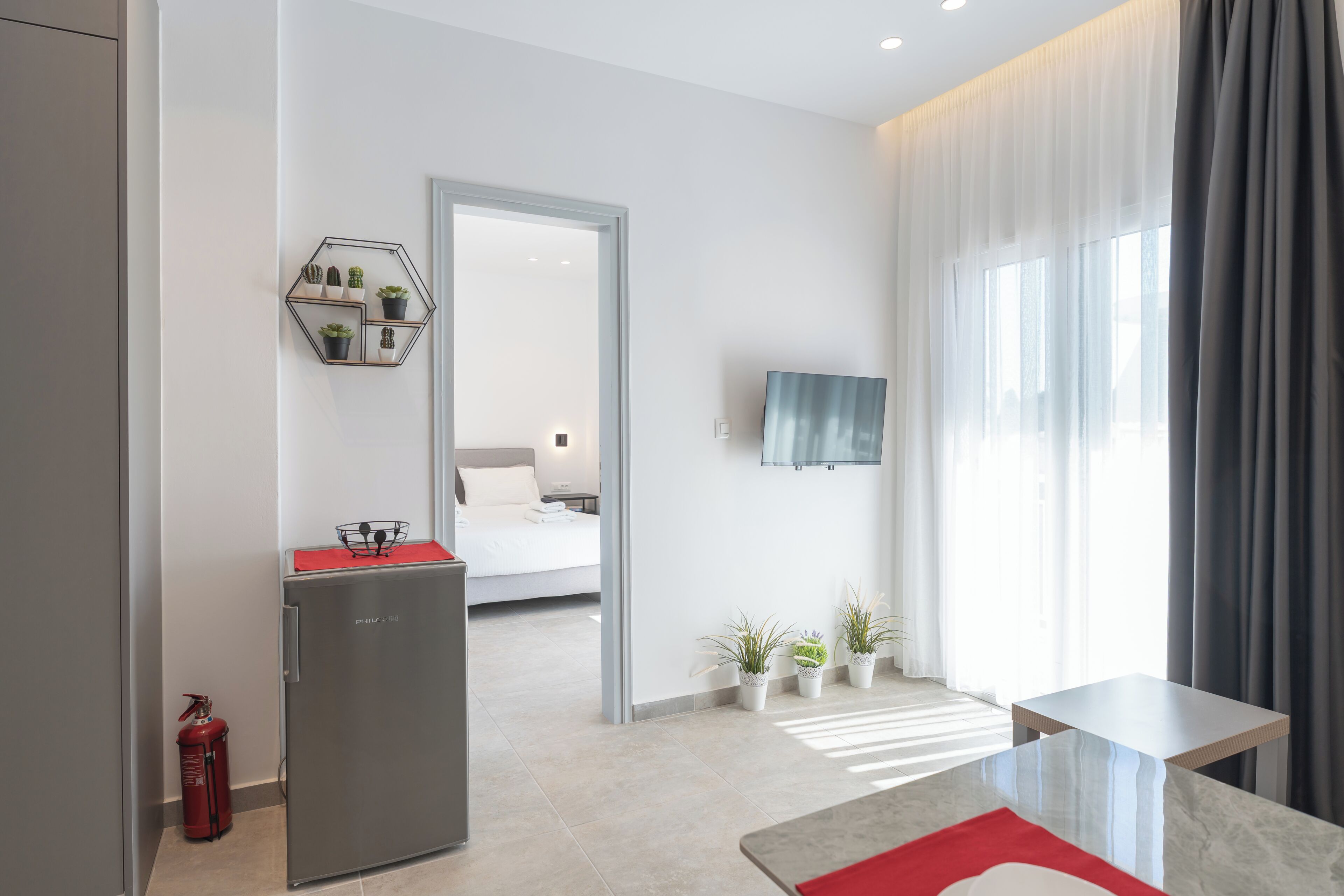 Ein modernes Hotelzimmer mit Bett, einer kleinen Küchenzeile, einem Fernseher und Blick ins Freie.
