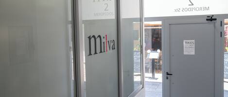 A glass door with the text 'Milva' and 'Meropidos St.' Another door has a sign stating 'Bikes are not allowed inside the building.'
