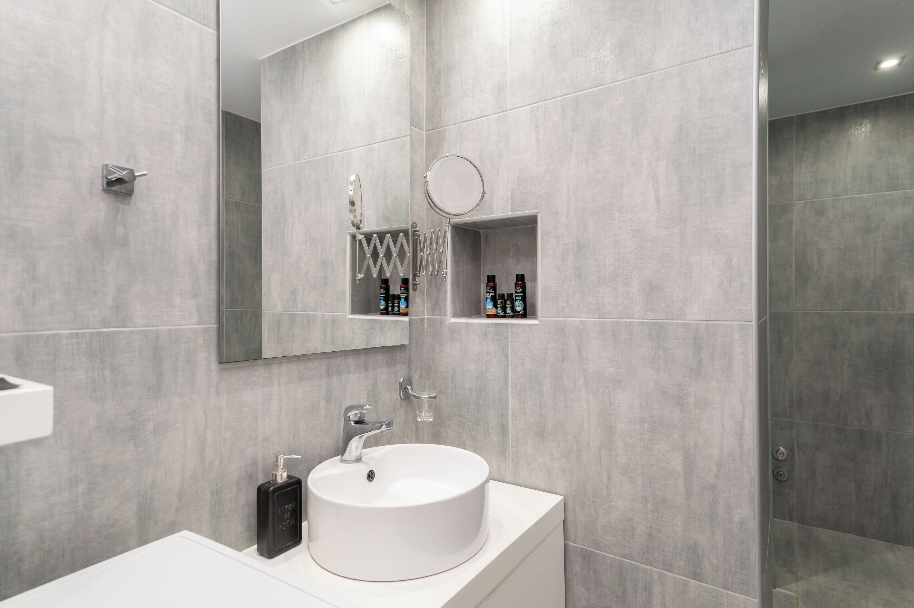 Een moderne badkamer met een wit wastafelmeubel, spiegel en inbouwplanken.