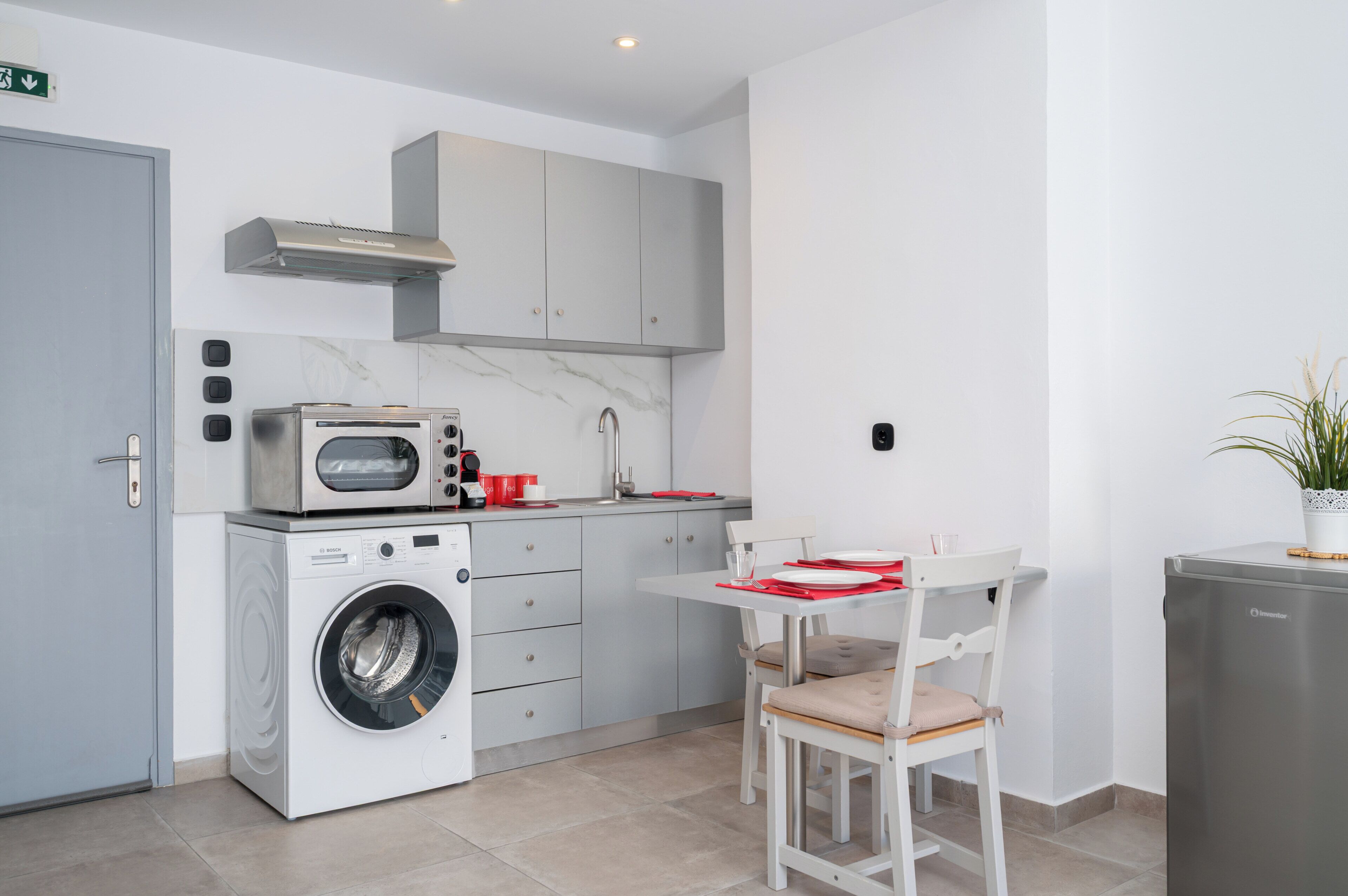 Cocina compacta con lavadora, microondas y un pequeño comedor con una silla y una mesa.