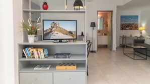 A modern living room with a television, books, and decorative items on shelves. - Milva Apartments (Kos)