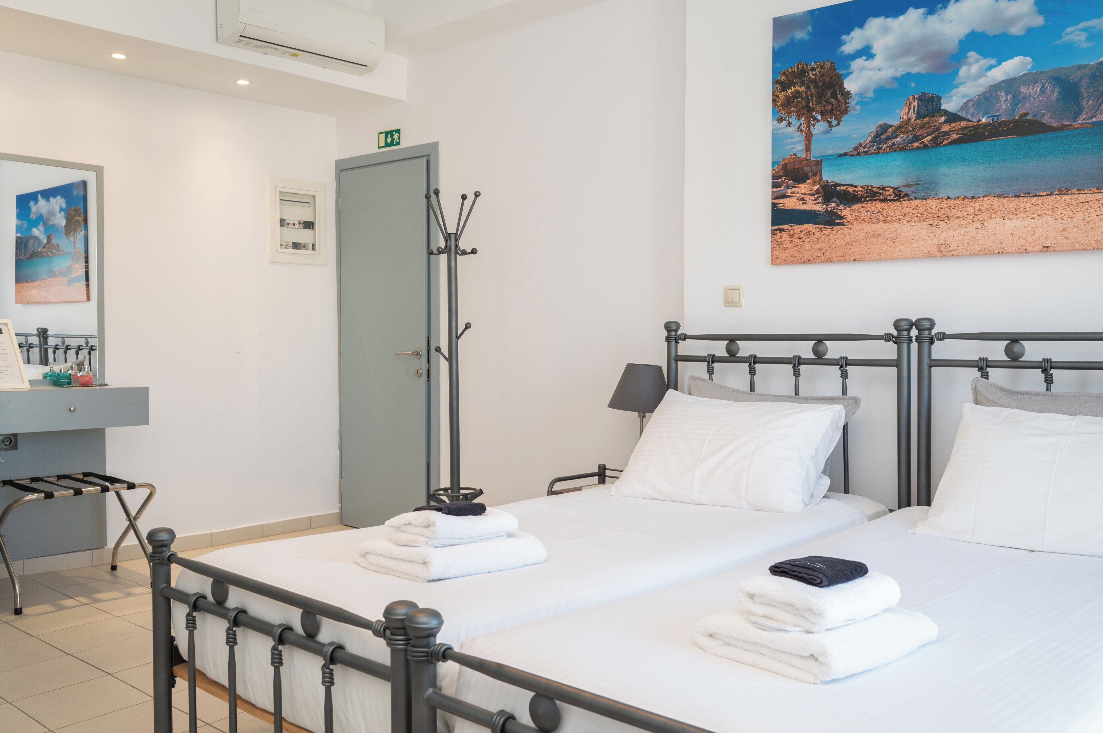 Una habitación de hotel con dos camas, un baño, un cuadro de una playa y vista al mar.