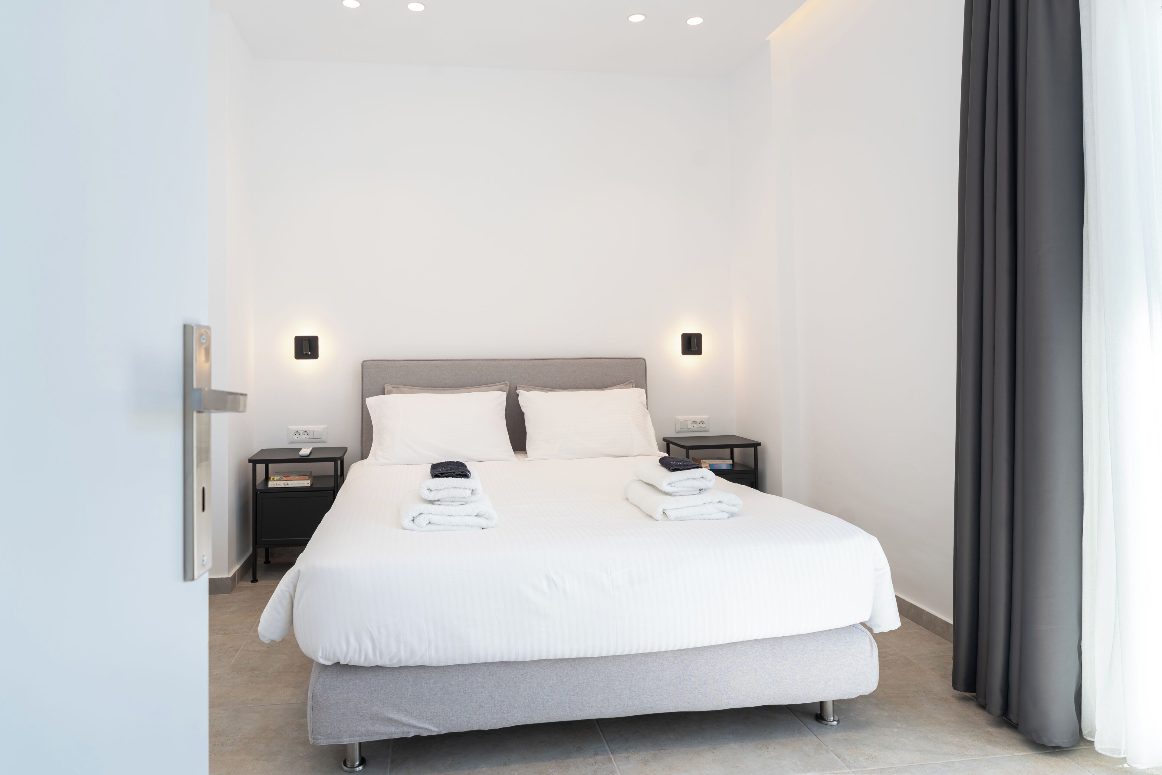 Una habitación de hotel moderna con una cama grande, dos mesitas de noche y una lámpara de pared.