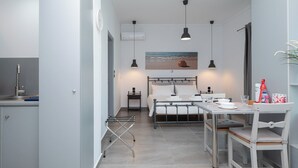 A modern kitchen with a dining area, a bed with a view, and a small table with chairs. - Milva Apartments (Kos)