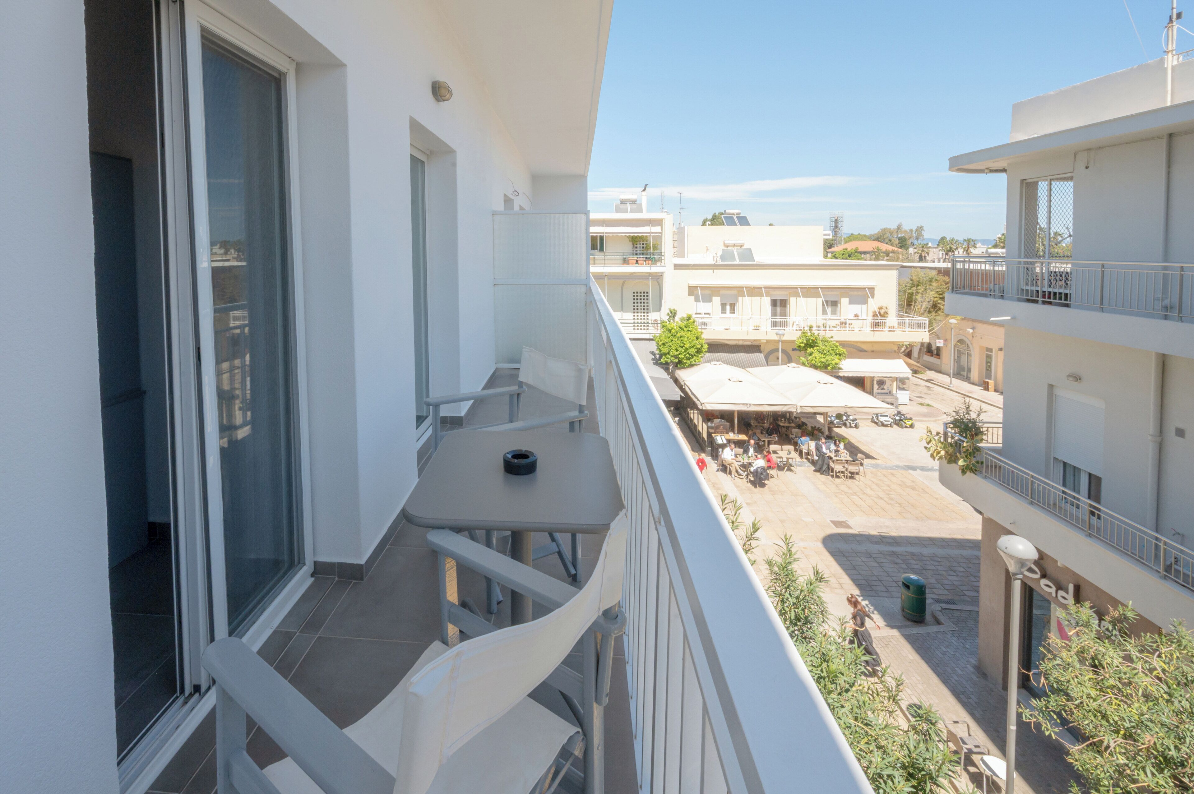 A balcony with a table and chairs, a view of a courtyard with outdoor seating, and a building with multiple floors and balconies.