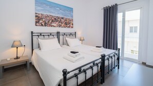 A bedroom with a bed, bedside tables, a lamp, a painting, and a view of the outside. - Milva Apartments (Kos)
