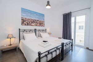 Un dormitorio con cama, mesitas de noche, lámpara, un cuadro y vistas al exterior.