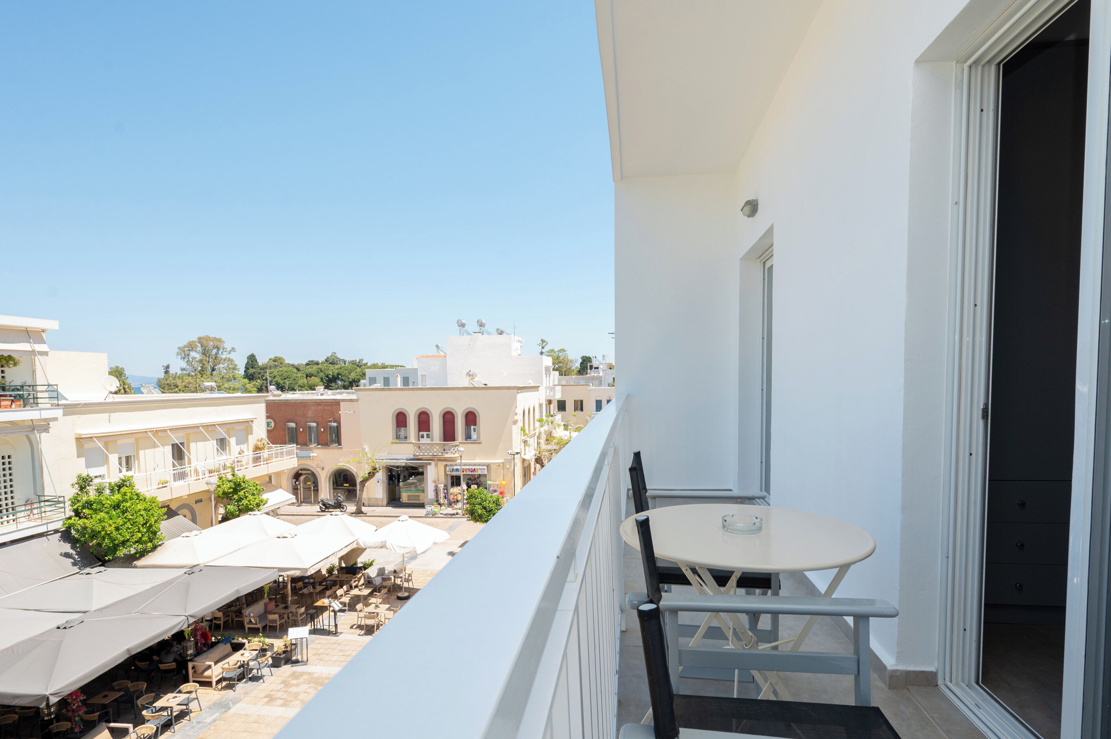 A balcony with a table and chairs, overlooking a street with buildings and outdoor seating.