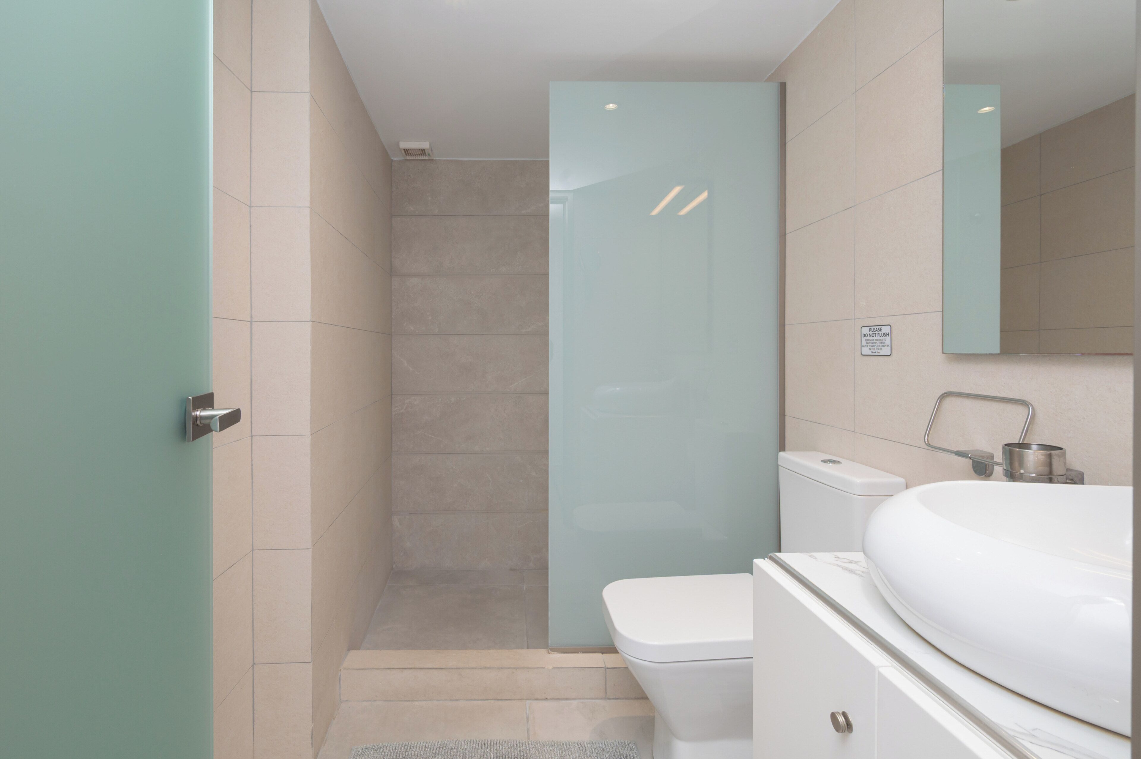 Un baño moderno con cabina de ducha de vidrio, inodoro blanco y un lavamanos grande con espejo superior.