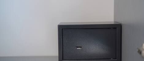 Un objeto negro, de forma cuadrada, con un pequeño rectángulo recortado en la parte frontal, apoyado sobre una pared lisa.