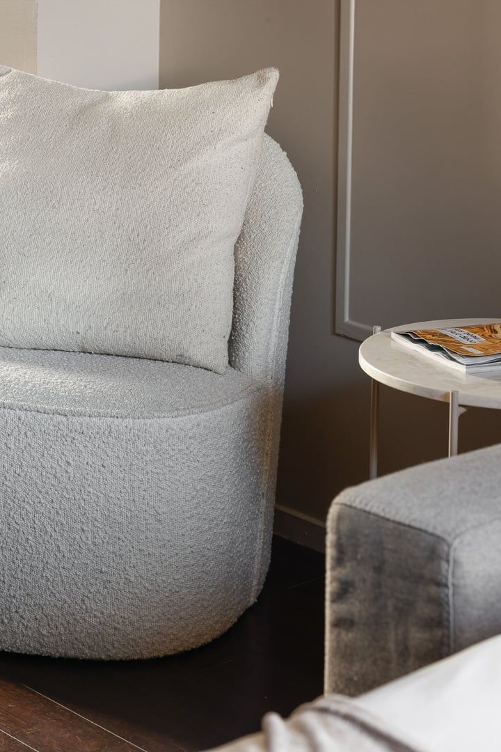 A round, plush armchair with a cushion, a small round table with a magazine, and a framed picture on the wall.