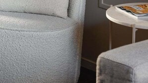 Un fauteuil rond et moelleux avec un coussin, une petite table ronde sur laquelle repose un magazine, et un tableau encadré accroché au mur.