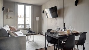 Un salon moderne comprenant un coin repas, un canapé, un téléviseur fixé au mur et un balcon avec une balustrade.