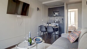 Un salon moderne doté d’un téléviseur à écran plat, d’un coin repas avec une table pour deux personnes et d’une kitchenette équipée d’un four à micro-ondes.