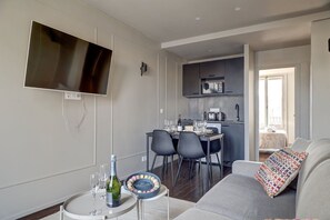 Una sala de estar moderna con un televisor de pantalla plana, un comedor con una mesa dispuesta para dos personas y una kitchenette con microondas.