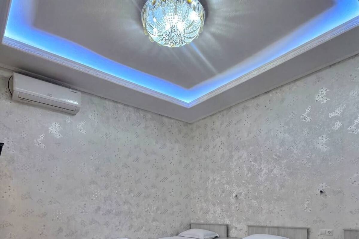 A hotel room with three beds, a wooden desk, a patterned rug, and a modern chandelier.
