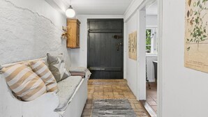 A narrow hallway with a white wall, a wooden door, a white sofa with striped cushions, and a black and white rug. - Peace and nature in a historic holiday home (Højer)