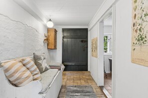 A narrow hallway with a white wall, a wooden door, a white sofa with striped cushions, and a black and white rug.