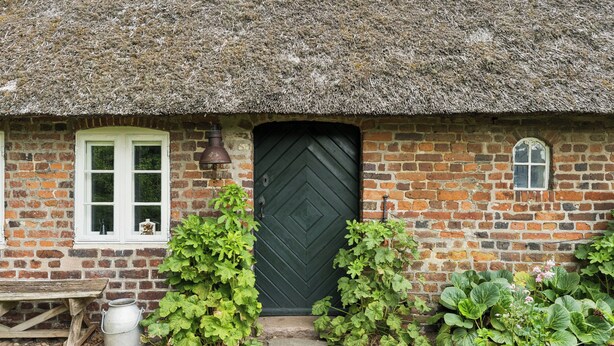 A brick house with a thatched roof, a green door, and a window with white shutters. - Peace and nature in a historic holiday home (Højer)