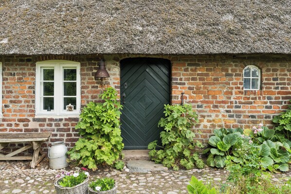 A brick house with a thatched roof, a green door, and a window with white shutters.