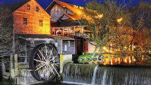 Un bâtiment historique abritant un ancien moulin, avec une grande roue à eau, une structure en bois portant une enseigne indiquant « Vieux Moulin », et une cascade.