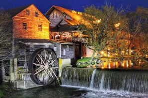 Un bâtiment historique abritant un ancien moulin, avec une grande roue à eau, une structure en bois portant une enseigne indiquant « Vieux Moulin », et une cascade.