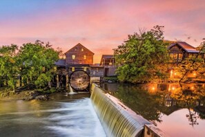 A watermill with a wooden structure and a large wheel, surrounded by trees and a calm river. - Walk to Dollywood fireworks view new 2025 Cozy 2-bedroom Private Hot Tub (Pigeon Forge)