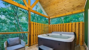 Une terrasse en bois avec un jacuzzi, une chaise en osier et une clôture en bois.