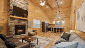 Un intérieur chaleureux de chalet en bois, avec une cheminée en pierre, des canapés en cuir, un coin repas et une cuisine.