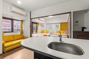 Ein Hotelzimmer mit einem großen Waschbecken, zwei Betten mit gelben Kissen, einer Couch und einer Klimaanlage.