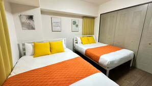 A hotel room with two beds, each with white bedding and orange blankets, a yellow curtain, and a closet with sliding doors. - Grace Nagahori 402 (Osaka)