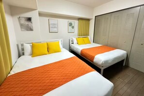 A hotel room with two beds, each with white bedding and orange blankets, a yellow curtain, and a closet with sliding doors. - Grace Nagahori 402 (Osaka)