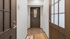 A narrow hallway with a wooden door at the end, a light switch, and a fire alarm on the wall. - Grace Nagahori 402 (Osaka)