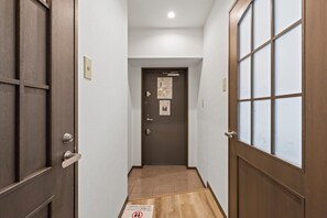 A narrow hallway with a wooden door at the end, a light switch, and a fire alarm on the wall. - Grace Nagahori 402 (Osaka)