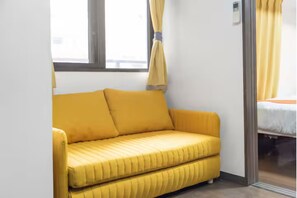 A small room with a yellow sofa, a window with curtains, and a bed with a white mattress. - Grace Nagahori 402 (Osaka)