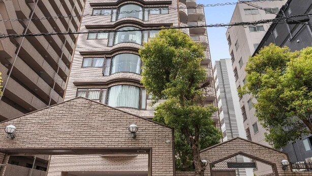 A multi-story building with a parking garage entrance, a tree, and a clear sky. - Grace Nagahori 402 (Osaka)