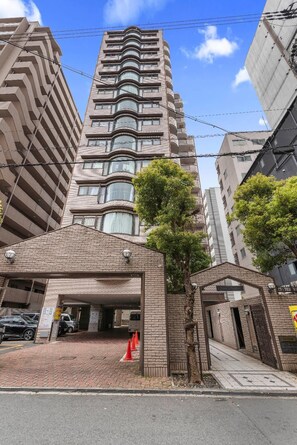 A multi-story building with a parking garage entrance, a tree, and a clear sky. - Grace Nagahori 402 (Osaka)