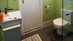 Un baño con inodoro blanco, paredes verdes, cabina de ducha de vidrio y lavamanos blanco con una toalla colgada.