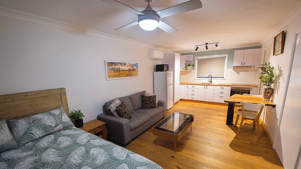 Un espacio habitable compacto con cama, sofá, mesa de centro, mesa de comedor y área de cocina.