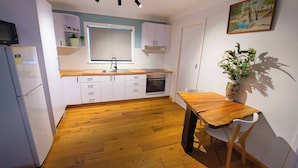 Una cocina compacta con armarios blancos, encimera de madera, horno empotrado y comedor con mesa y sillas de madera.