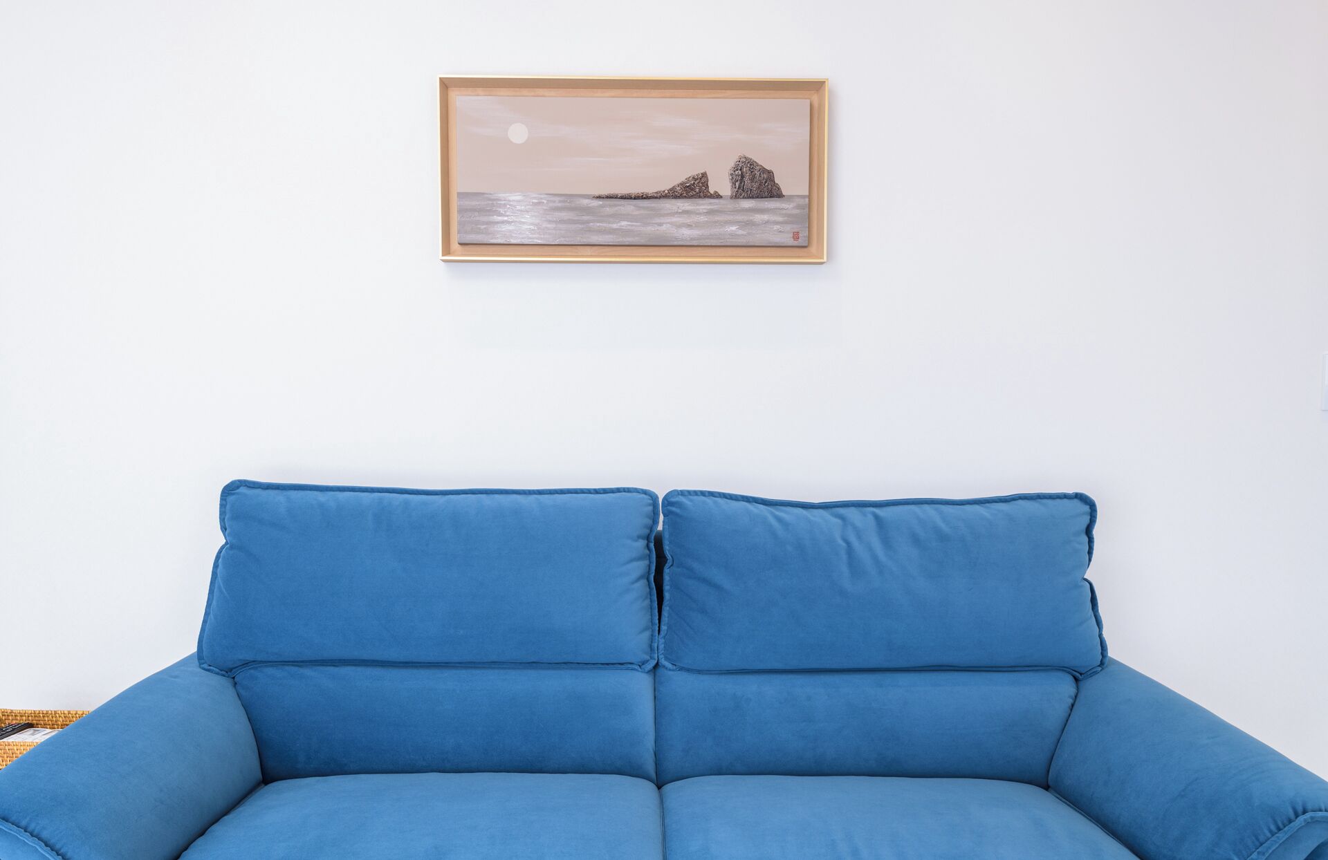 A blue sofa with a framed painting of a landscape above it.
