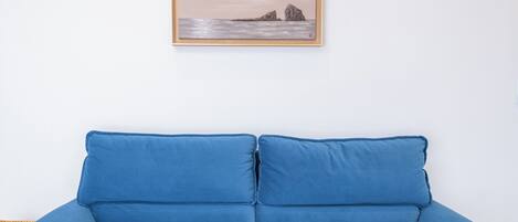 A blue sofa with a framed painting of a landscape above it.