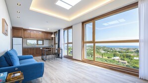A spacious living area with a large window, wooden flooring, and a blue sofa. - Brodick Jeju  (Seogwipo)